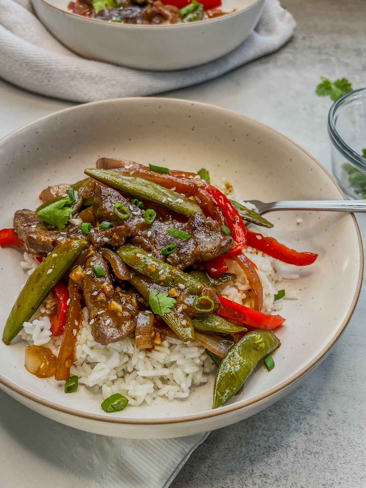 One pot sticky orange beef stir fry scooped into bowls over rice with some cilantro, green onion, and sesame seeds on top