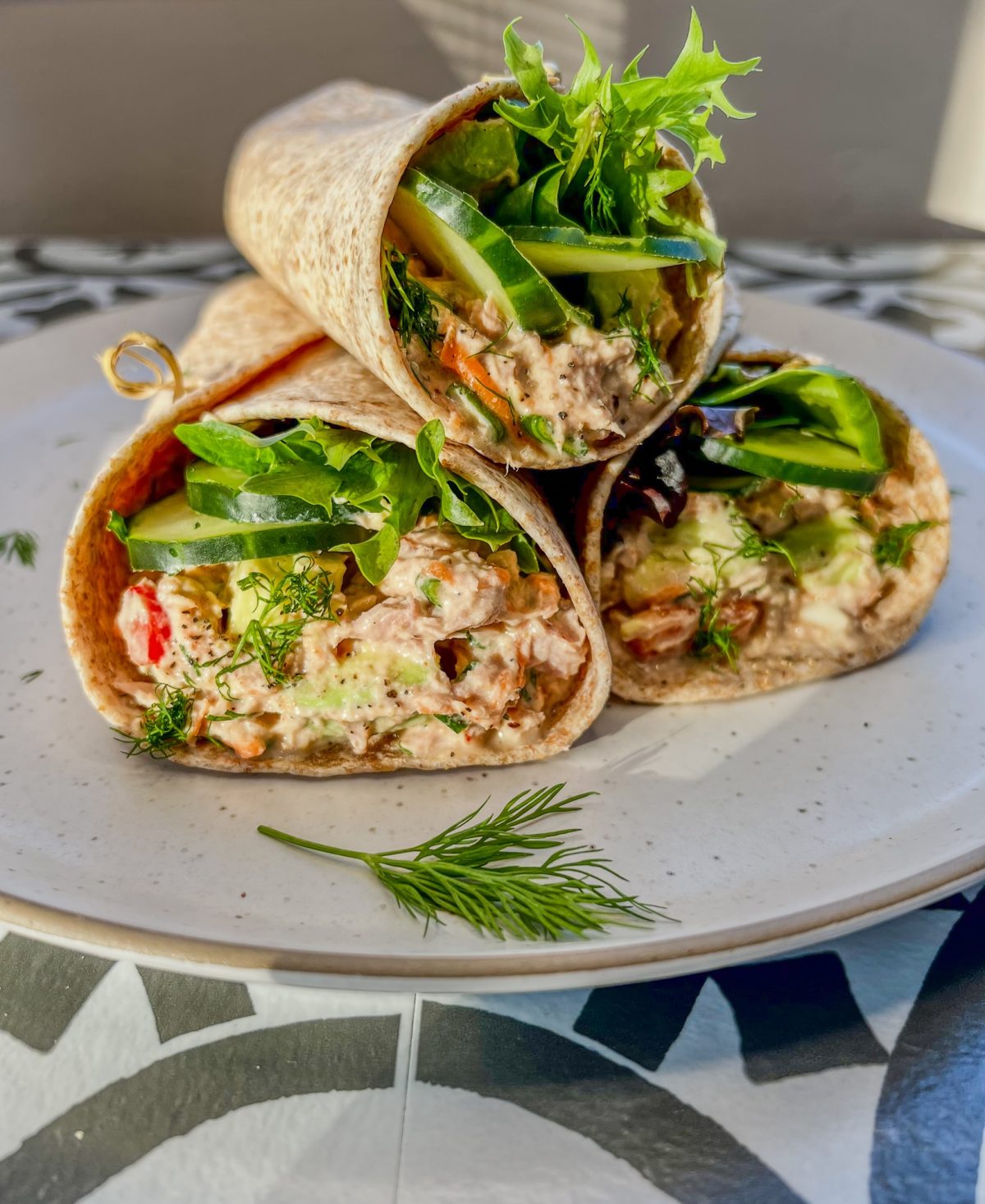 Tuna avocado wraps stacked up on a plate with some fresh dill sprinkled on top