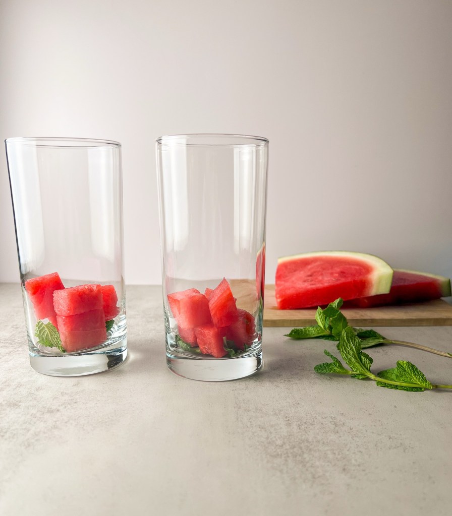 Two glasses with mint and watermelon in them before being muddled