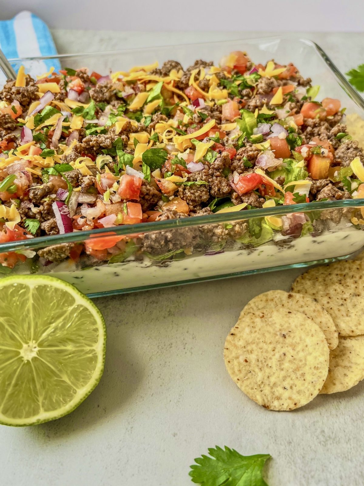 Beefy taco dip that's been freshly made and chilled served with fresh cilantro, lime, and some tortilla chips on the side
