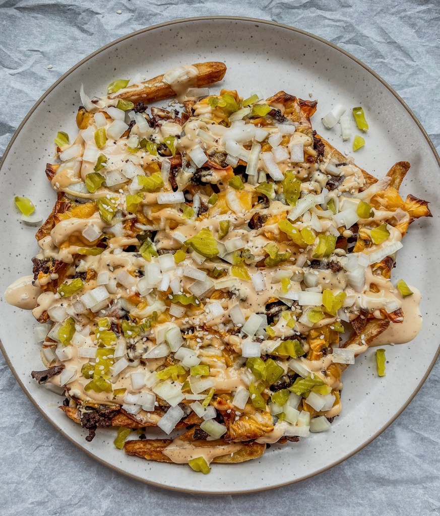 Cheesy smashburger fries with a Big Mac-style sauce, onion, dill pickles, and sesame seeds garnished on top.