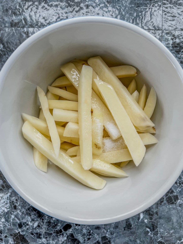 Raw homemade French fries in a bowl with some oil and salt