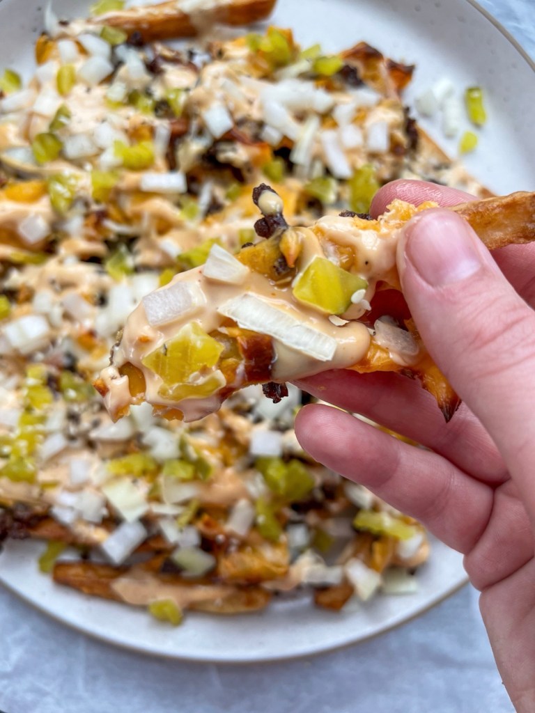 Cheesy smashburger fries with a Big-Mac style sauce drizzled on top and some pickle, onion, and sesame seeds for garnish