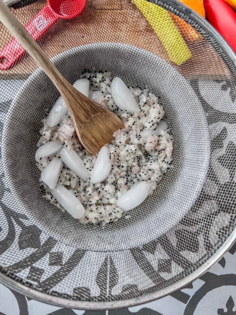 Dragon fruit rum cooler being strained through a fine mesh sieve
