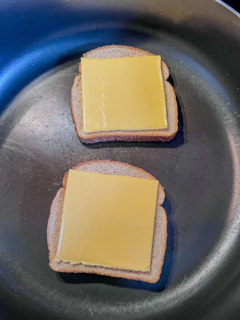 Buttered bread in a skillet with some sliced cheese on top