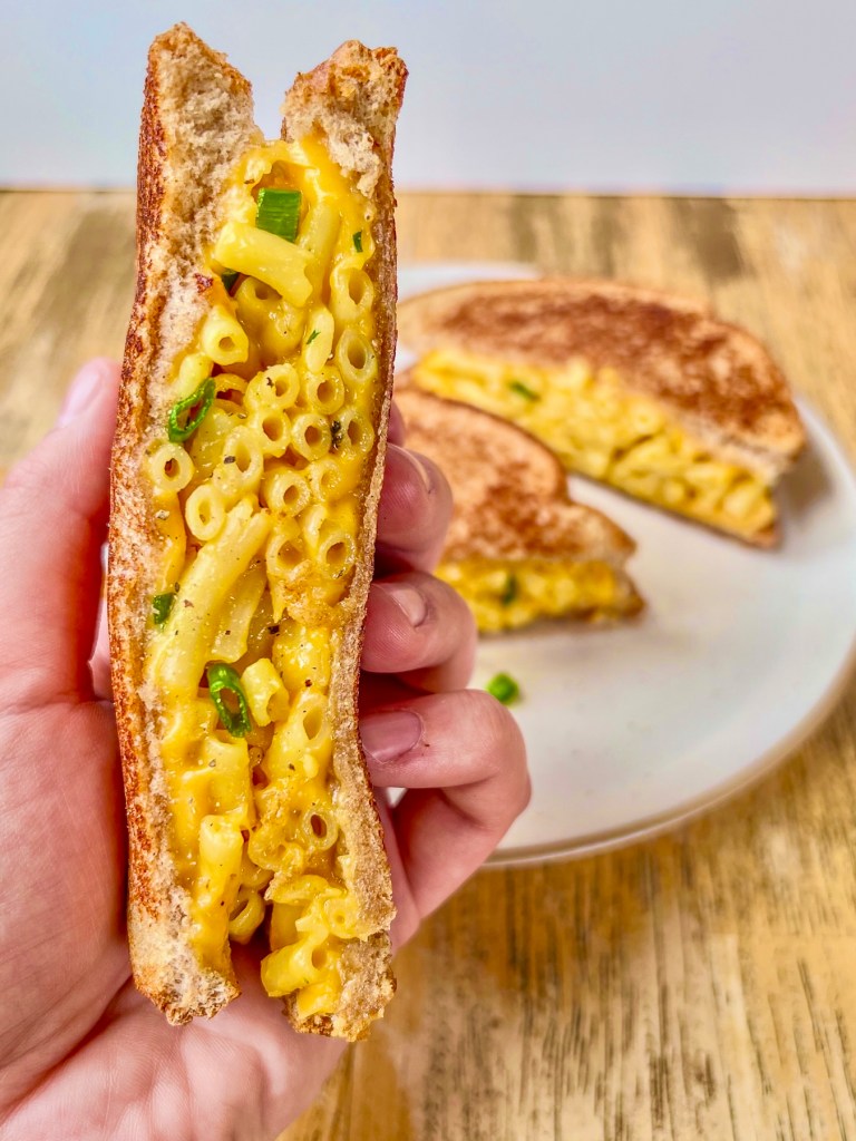 A grilled mac and cheese sandwich that's been sliced in half with some green onion and freshly cracked black pepper sprinkled on top