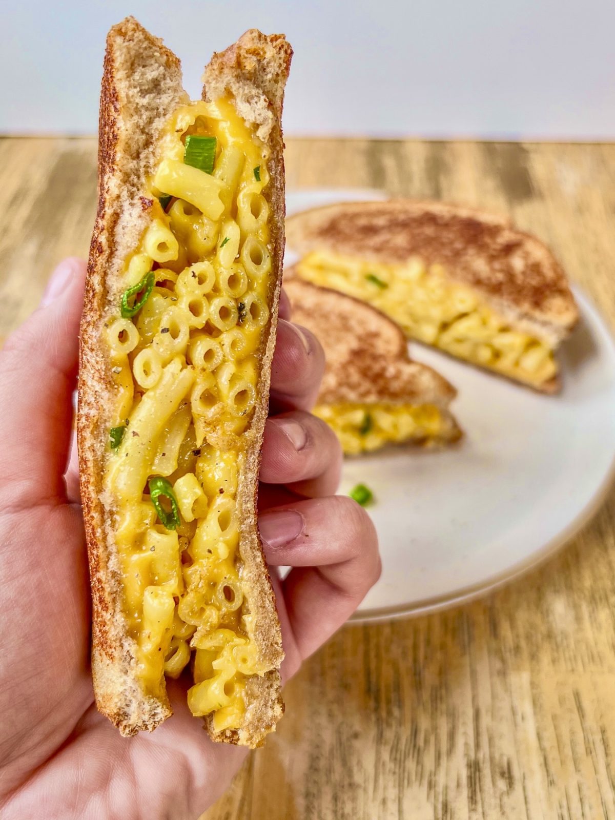 A grilled mac and cheese sandwich that's been sliced in half with some green onion and freshly cracked black pepper sprinkled on top