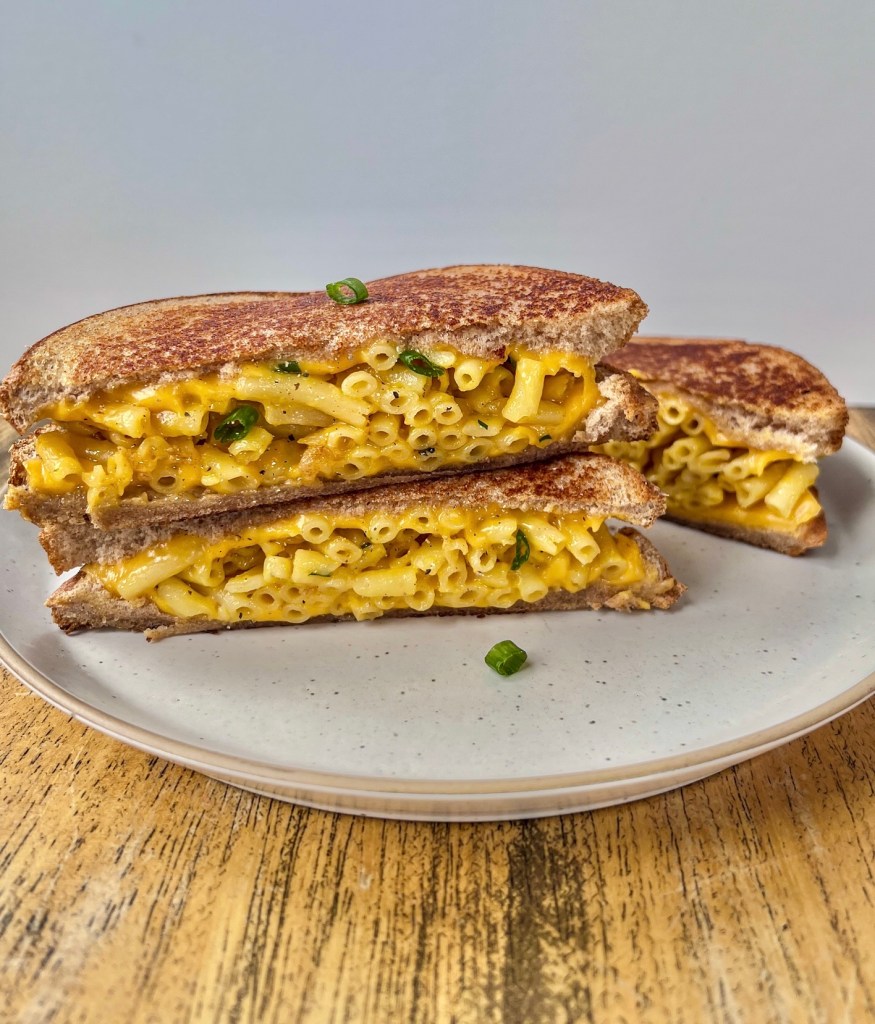 Grilled mac and cheese sandwiches that have been sliced in half and topped with freshly cracked black pepper and green onion