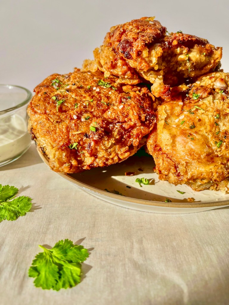 Hot honey fried chicken thighs with red pepper flakes, flaky salt, and minced cilantro on top with some dipping sauce on the side