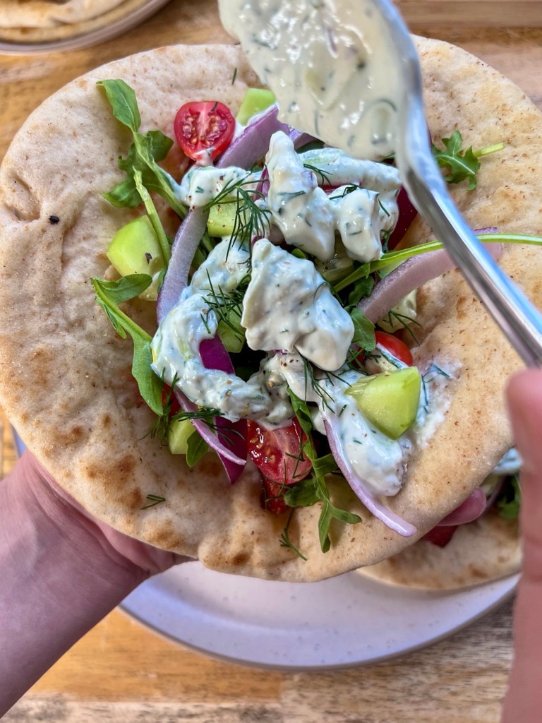 Smoked andouille sausage gyros fully assembled with some homemade tzatziki sauce being drizzled on top