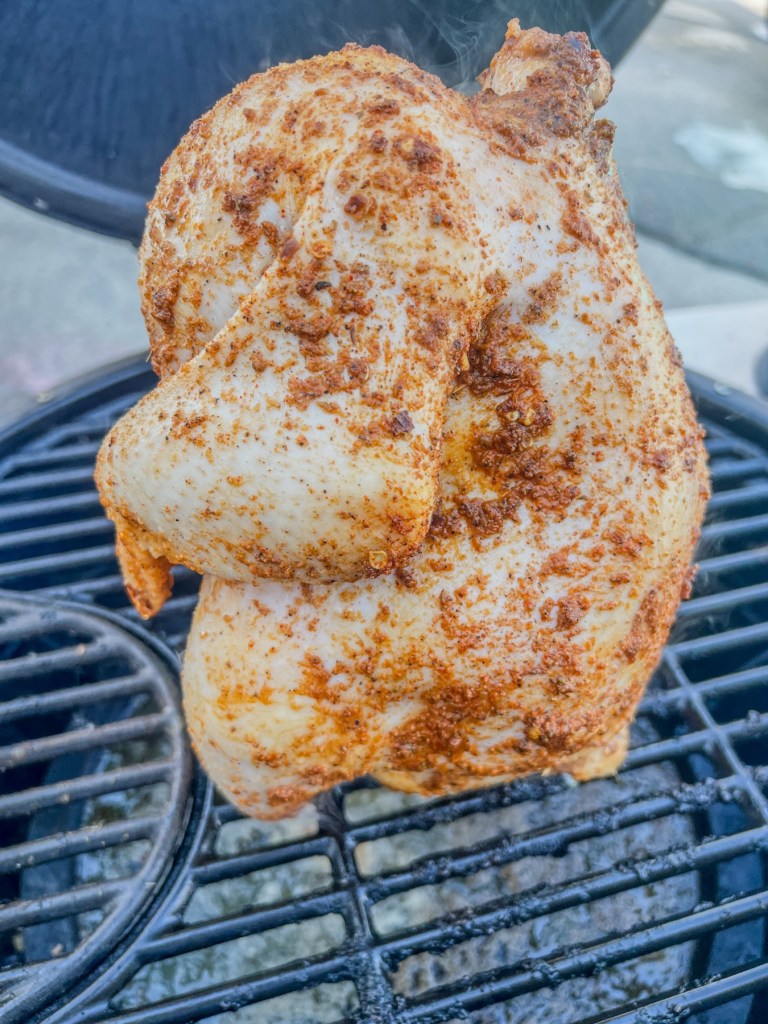 A whole chicken that's been rubbed with oil and spices, then placed on a charcoal grill to be smoked