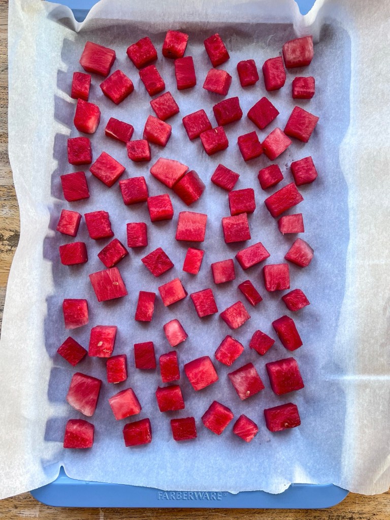 Watermelon cubes on a baking sheet lined with parchment paper just before going into the freezer