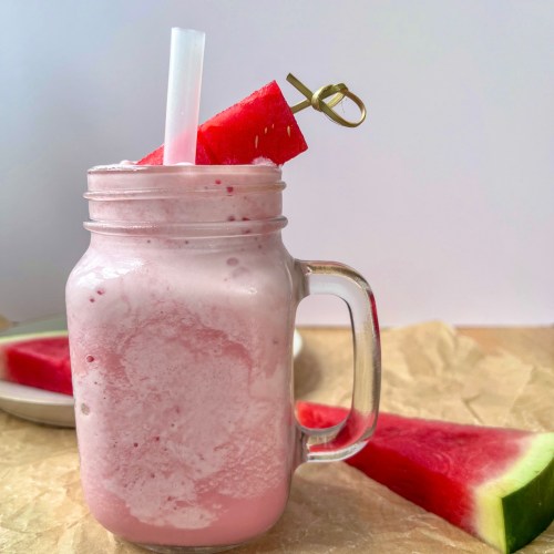 Watermelon cloud slushie in a glass with a thick straw and a skewer with watermelon cubes for garnish