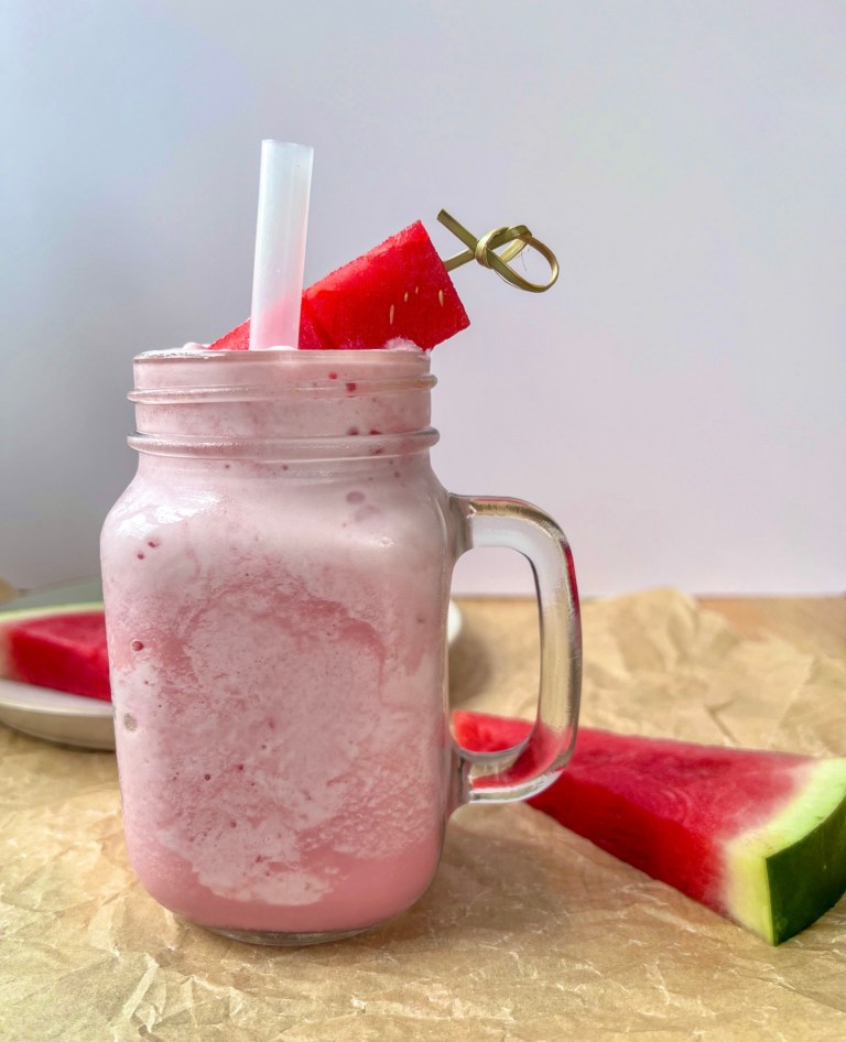 Watermelon cloud slushie in a glass with a thick straw and a skewer with watermelon cubes for garnish