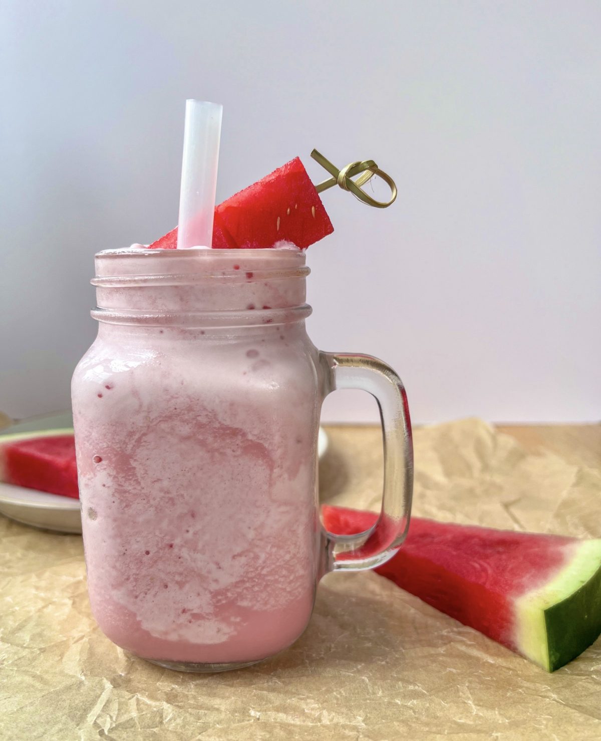 Watermelon cloud slushie in a glass with a thick straw and a skewer with watermelon cubes for garnish