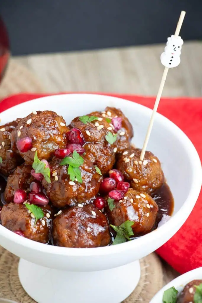Pomegranate meatball appetizers in a serving dish with fresh pomegranate seeds garnished on top