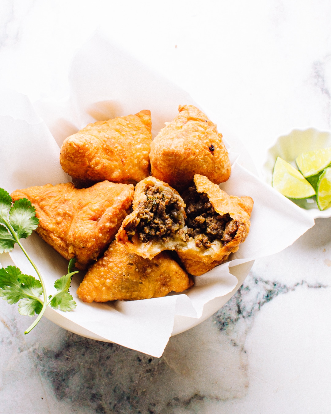 Taco samosas in a serving boat with some fresh herbs on the side