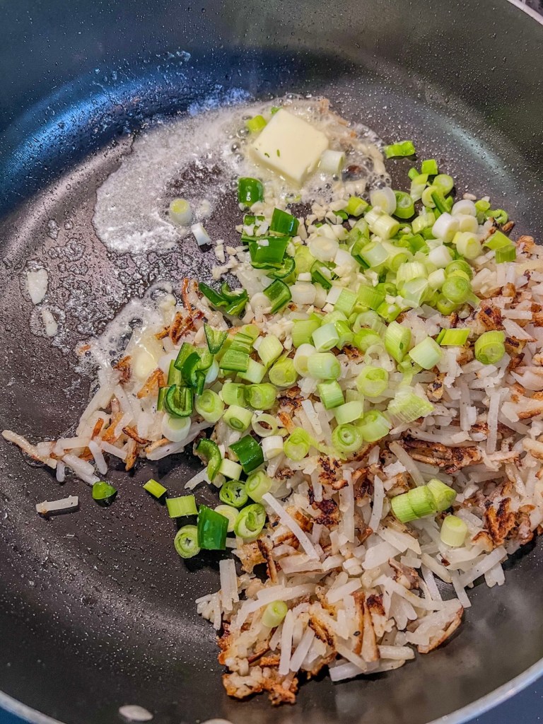 Hashbrowns, onion, garlic, serrano pepper, and butter cooking in a skillet