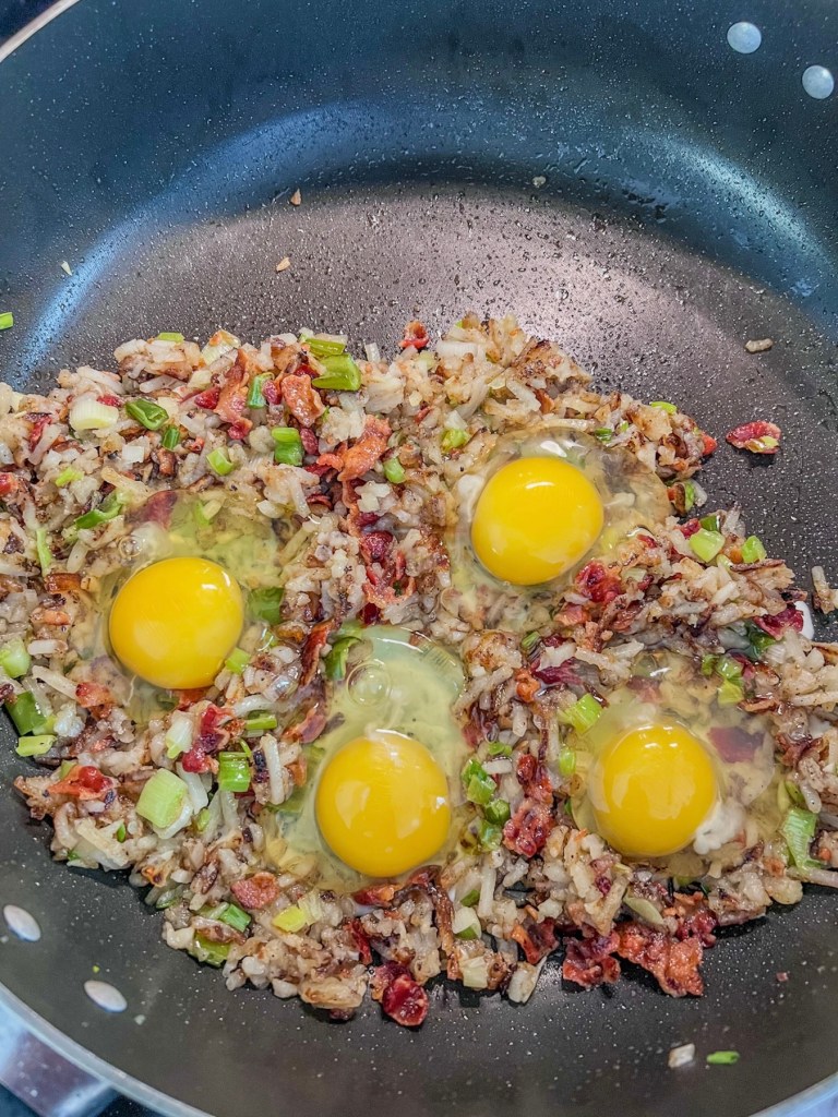 Hashbrowns, veggies, and eggs cooking in a skillet