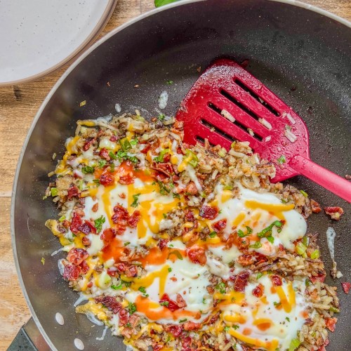 Bacon breakfast skillet in a pan with some crumbled bacon and fresh cilantro scattered off to the side