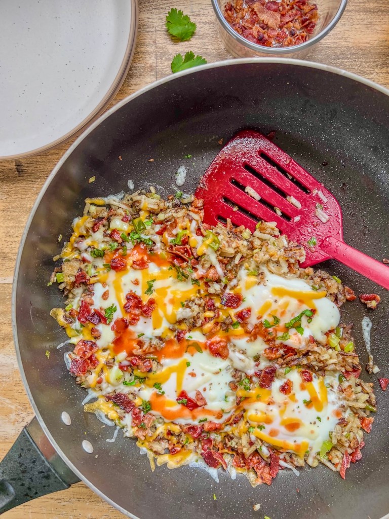 Bacon breakfast skillet in a pan with some crumbled bacon and fresh cilantro scattered off to the side