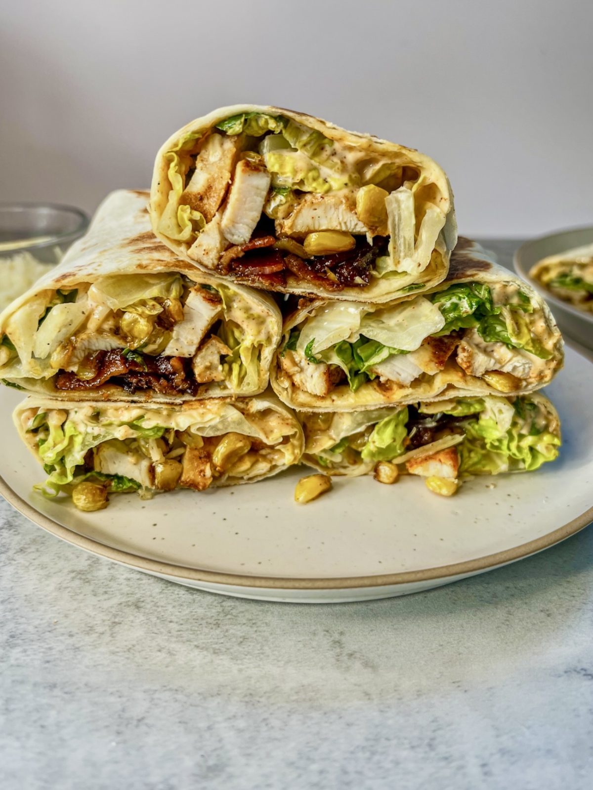 Bacon jam chicken Caesar salad wraps that have been sliced in half and stacked on a plate