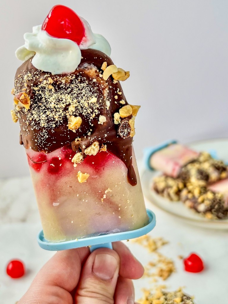 Banana split frozen yogurt pops with whipped cream and a maraschino cherry on top