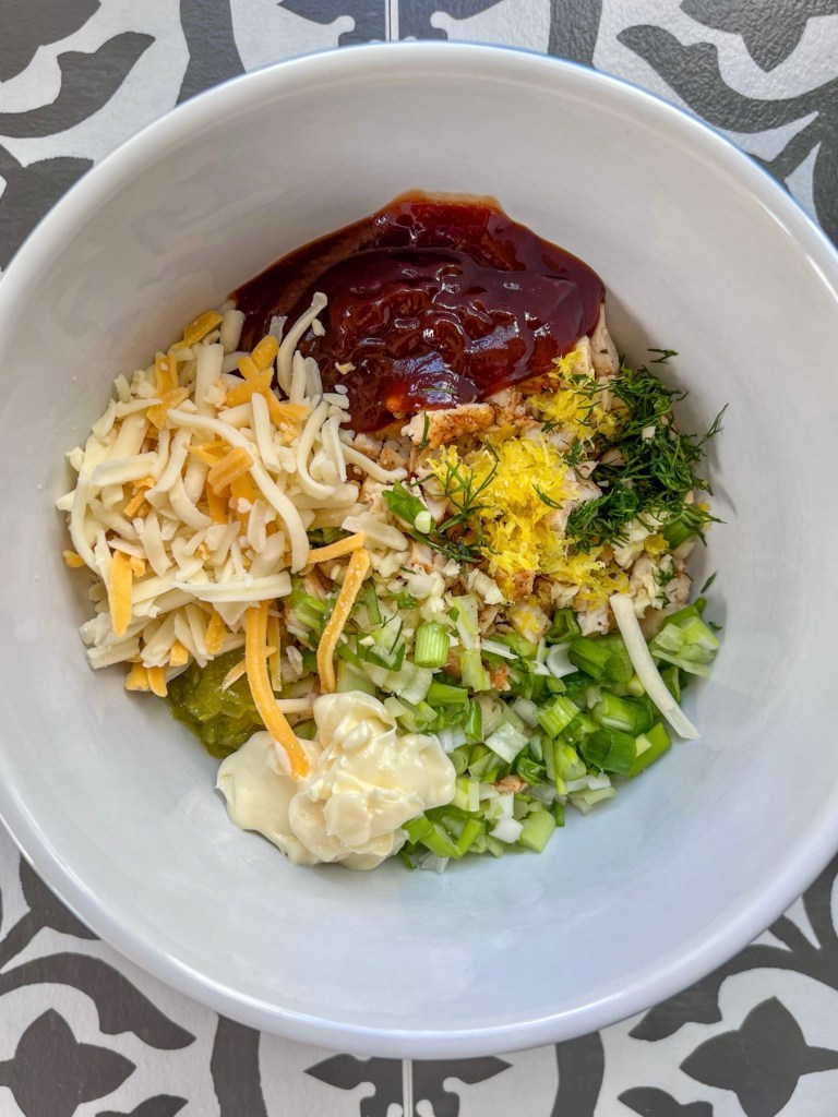 Mayo, bbq sauce, shredded cheddar, lemon zest and juice, green onion, and spices in a mixing bowl with some chopped chicken