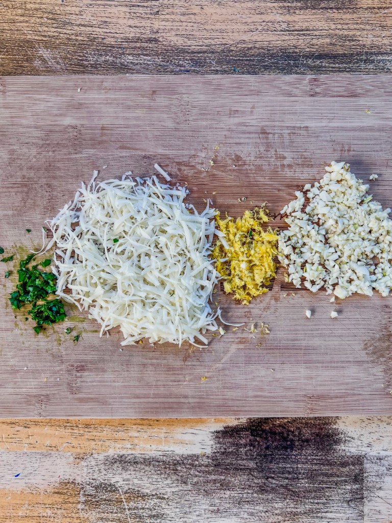 Parmesan cheese, garlic, lemon zest, and parsley prepped on a cutting board