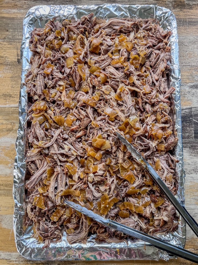 A large baking sheet filled with pulled pork carnita meat just before going in the oven for broiling
