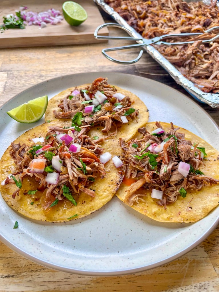 Crockpot pulled pork carnitas on a plate served as tacos with some more fixings off to the side