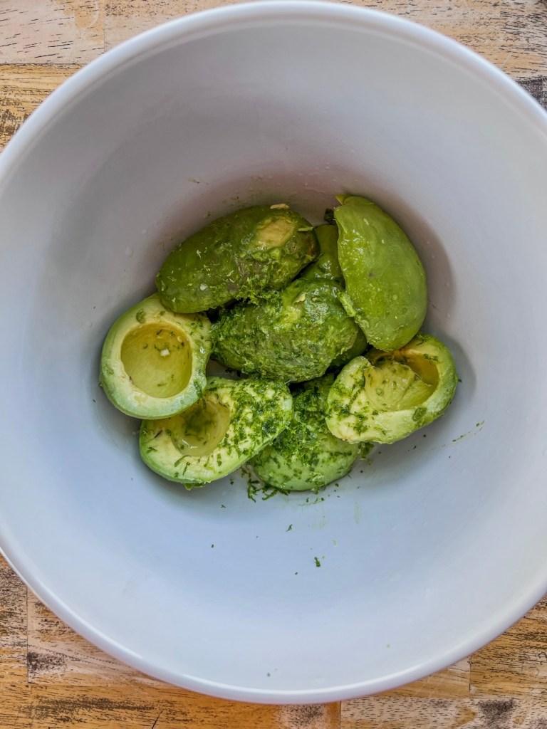 Avocados that have been peeled and pitted, then added to a bowl and topped with lime juice and zest