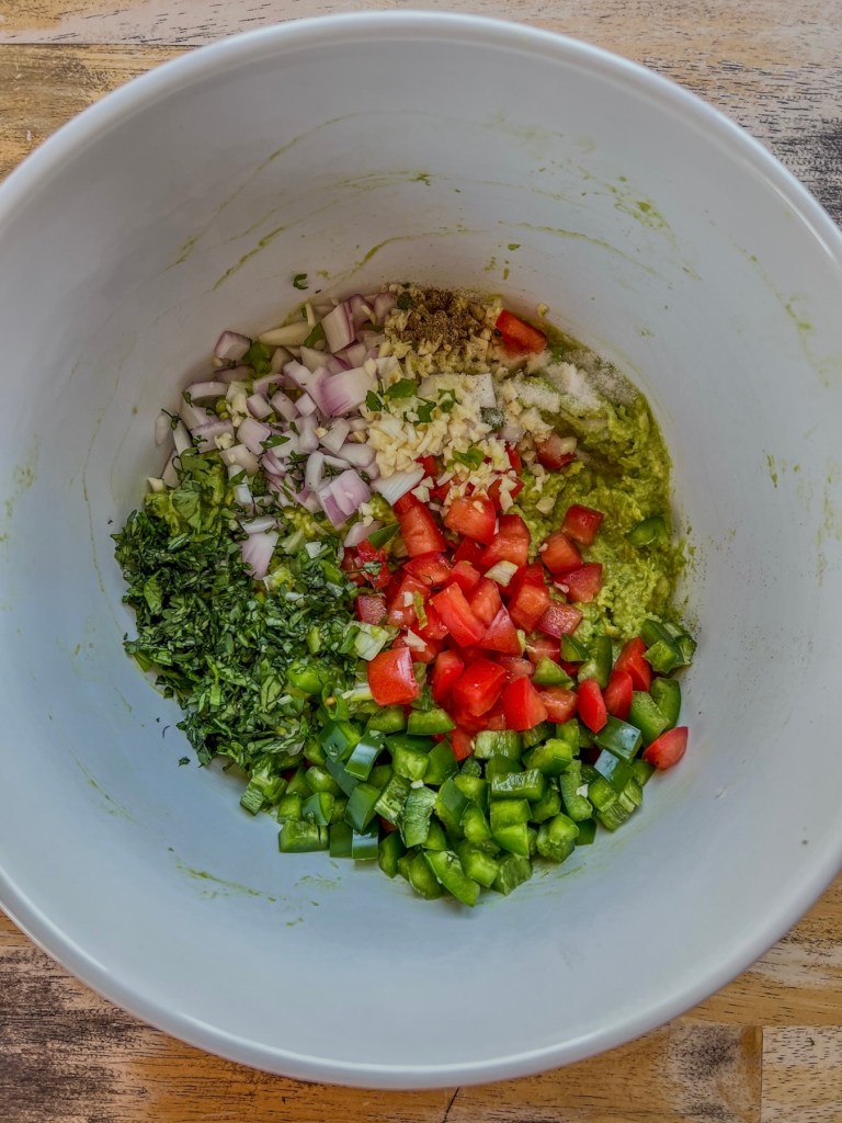 Ingredients for an easy guacamole dip in a mixing bowl before being stirred and chilled