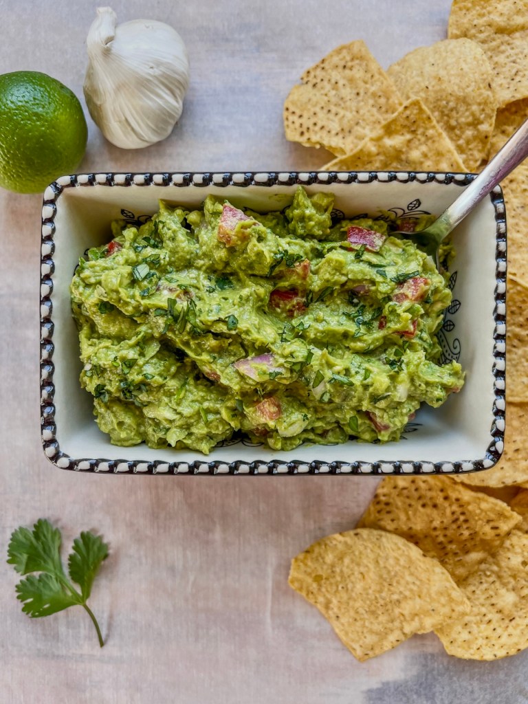 Easy guacamole dip served with tortilla chips and some more cilantro and lime on the side