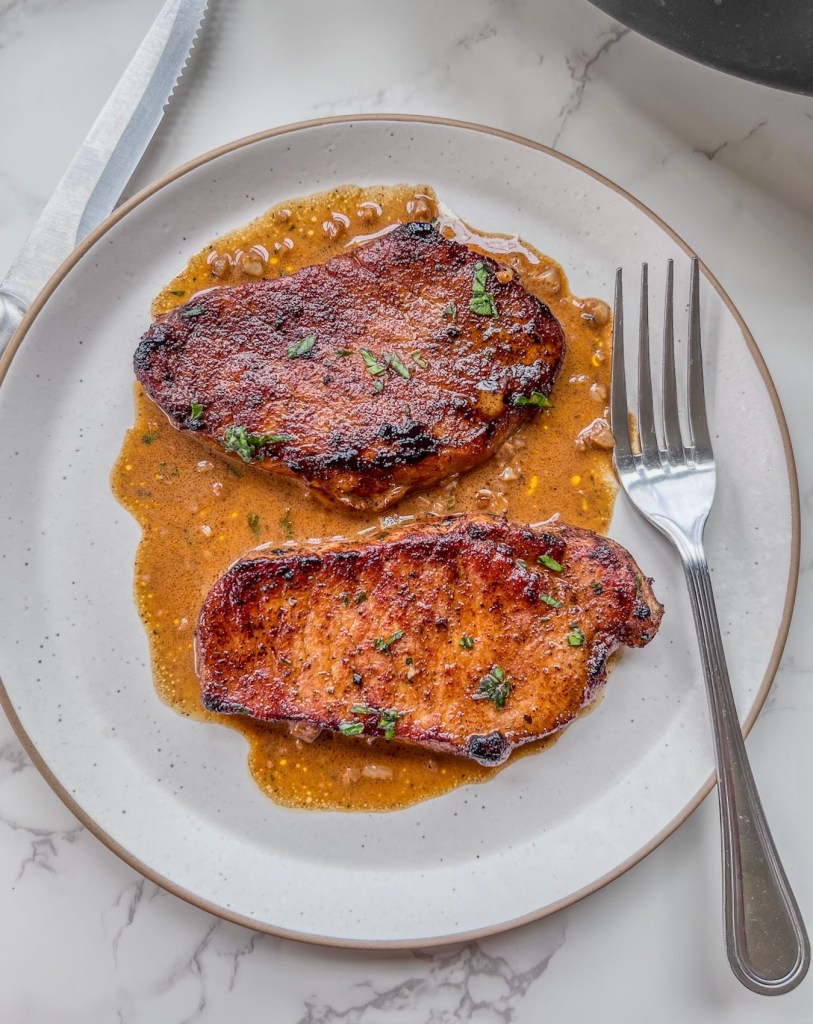 Espresso rubbed pork chops with creamy garlic sauce spooned over top and some fresh parsley for garnish