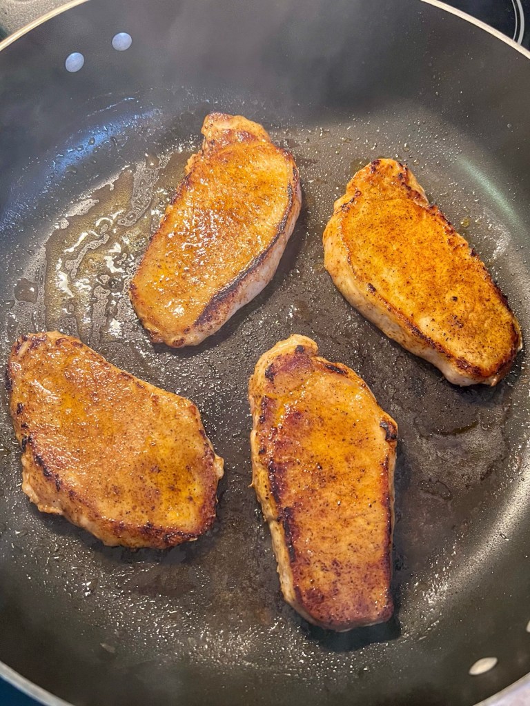 Pork chops being seared over medium high heat in a skillet