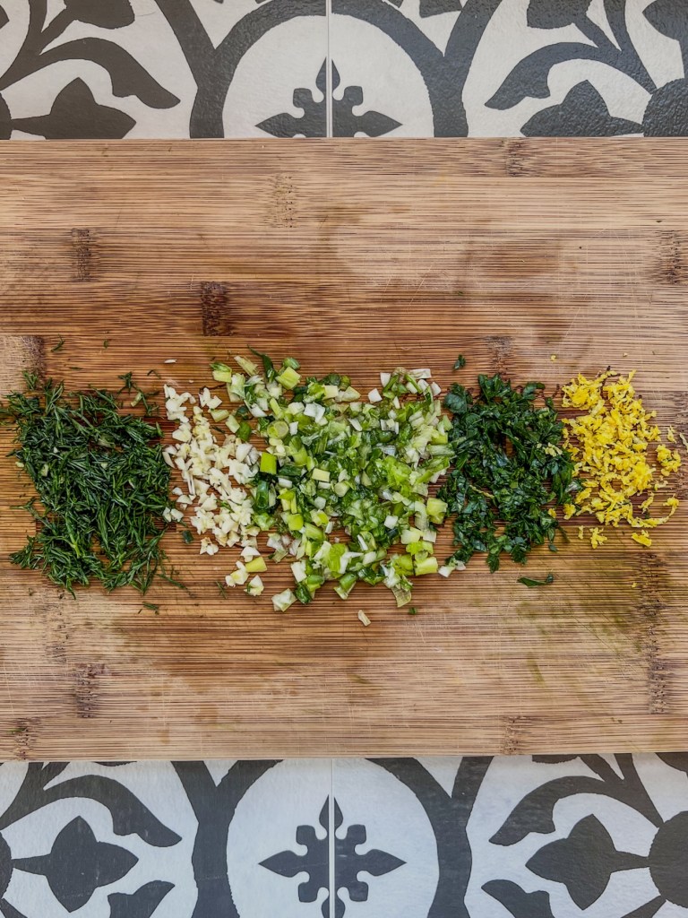 Lemon zest, dill, green onion, garlic, and parsley prepped on a cutting board