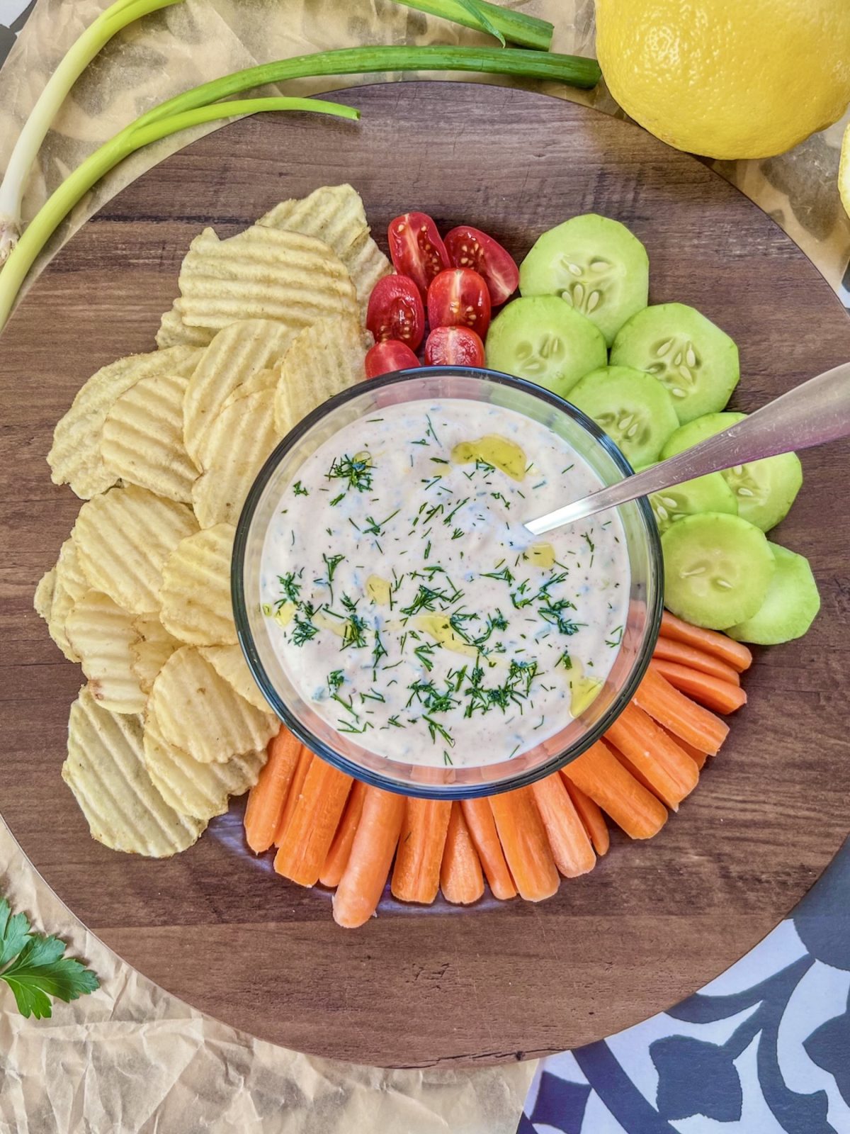 Lemon herb chip and veggie dip in a small bowl with a platter filled with veggies and chips surrounding it