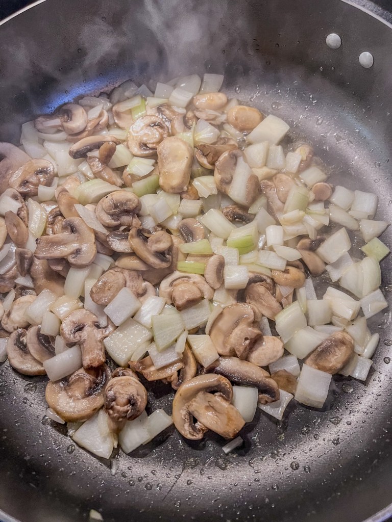 Diced yellow onion and sliced white mushrooms cooking in a skillet