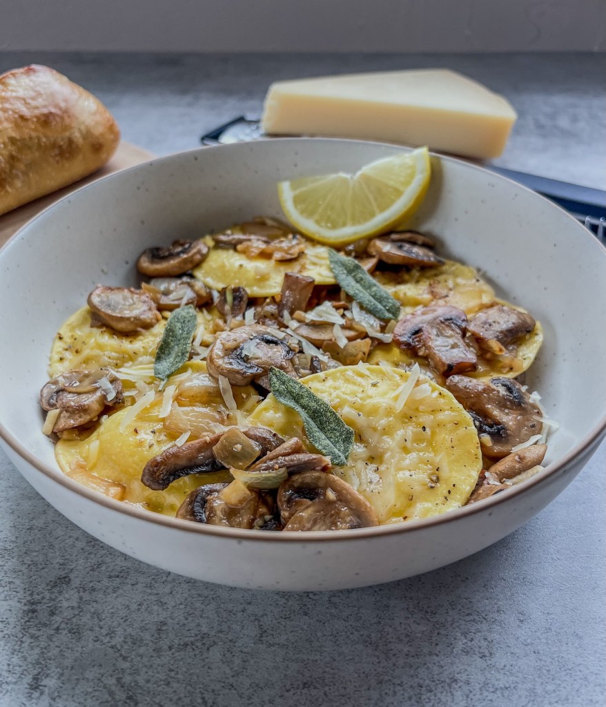 Ravioli with brown butter mushrooms and crispy sage in a bowl with some bread and parmesan off to the side