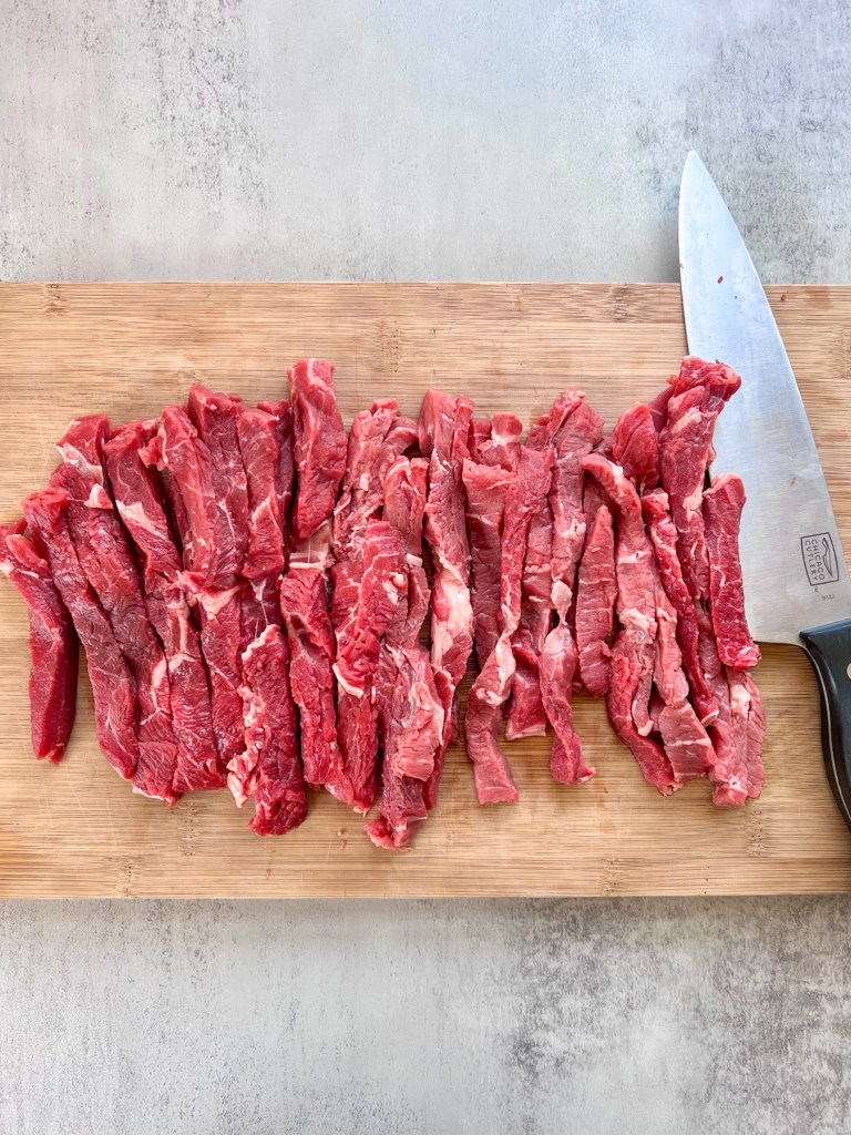 Sirloin steak cut into thin strips on a cutting board