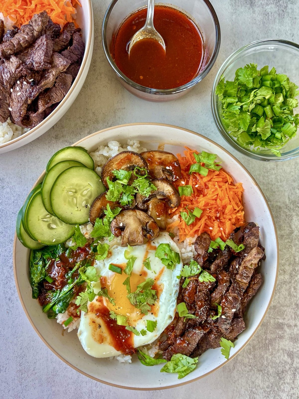 Steak bibimbap in a bowl with some carrots, cucumber, herbs, egg, and lemon gochujang glaze
