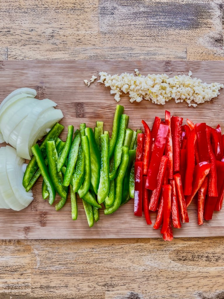 Onion, red and green bell pepper, and garlic prepped on a cutting board
