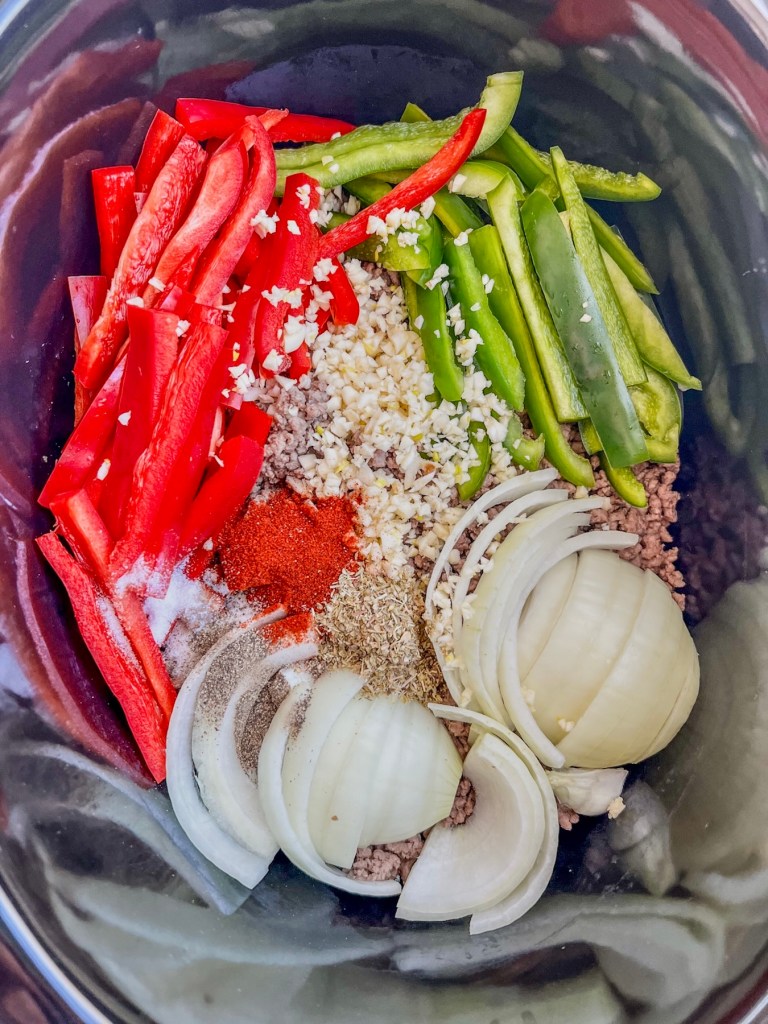 Bell pepper, onion, ground beef, broth, and spices in a crockpot just before cooking