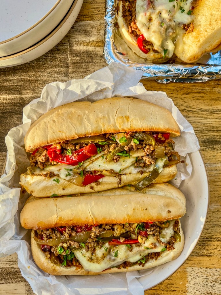Crockpot Philly cheesesteak sandwiches in a bowl with a tray of more off to the side