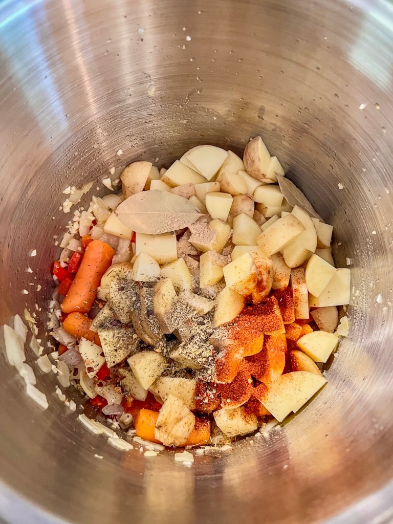 A stockpot filled with veggies, spices, and bay leaves.