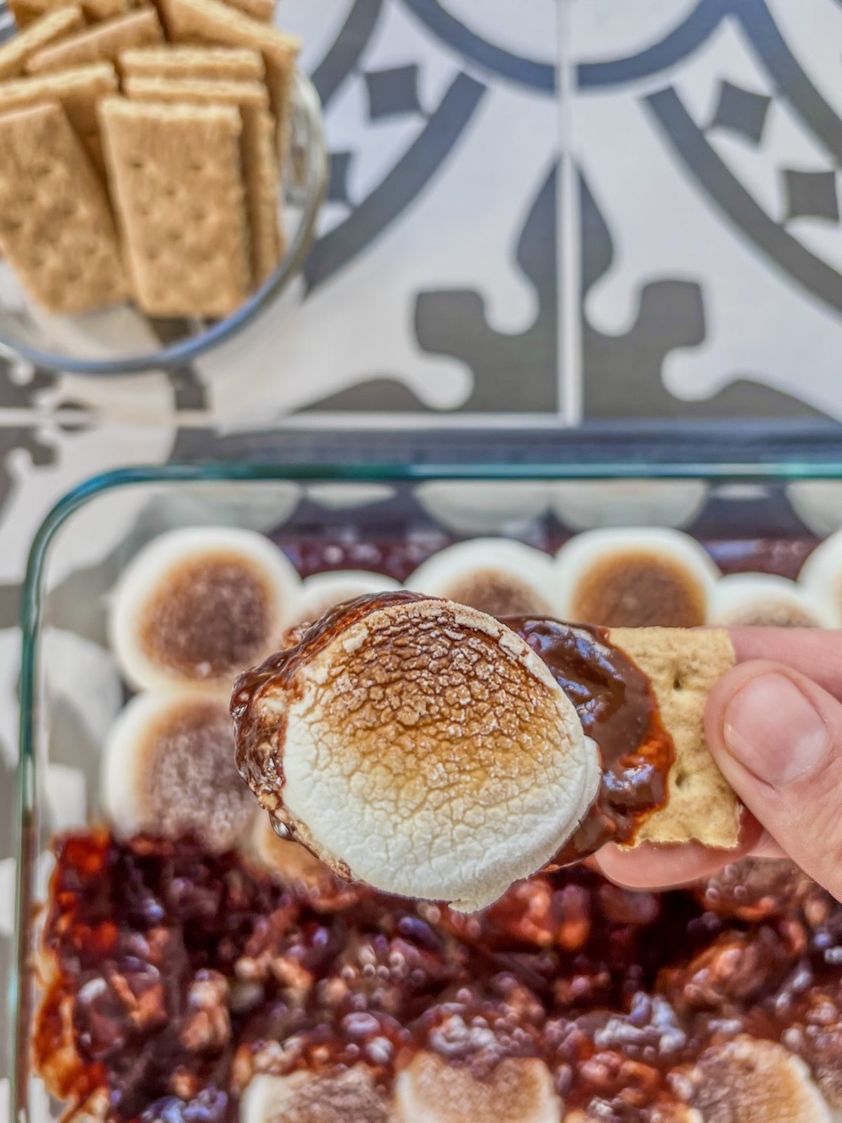 Oven s'mores dip fresh out of the oven, being scooped with a graham cracker