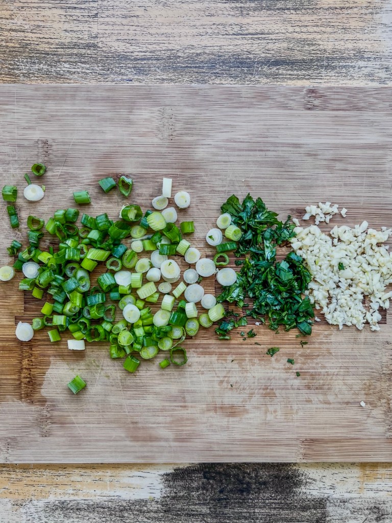 Cilantro, green onion, and garlic chopped up on a cutting board