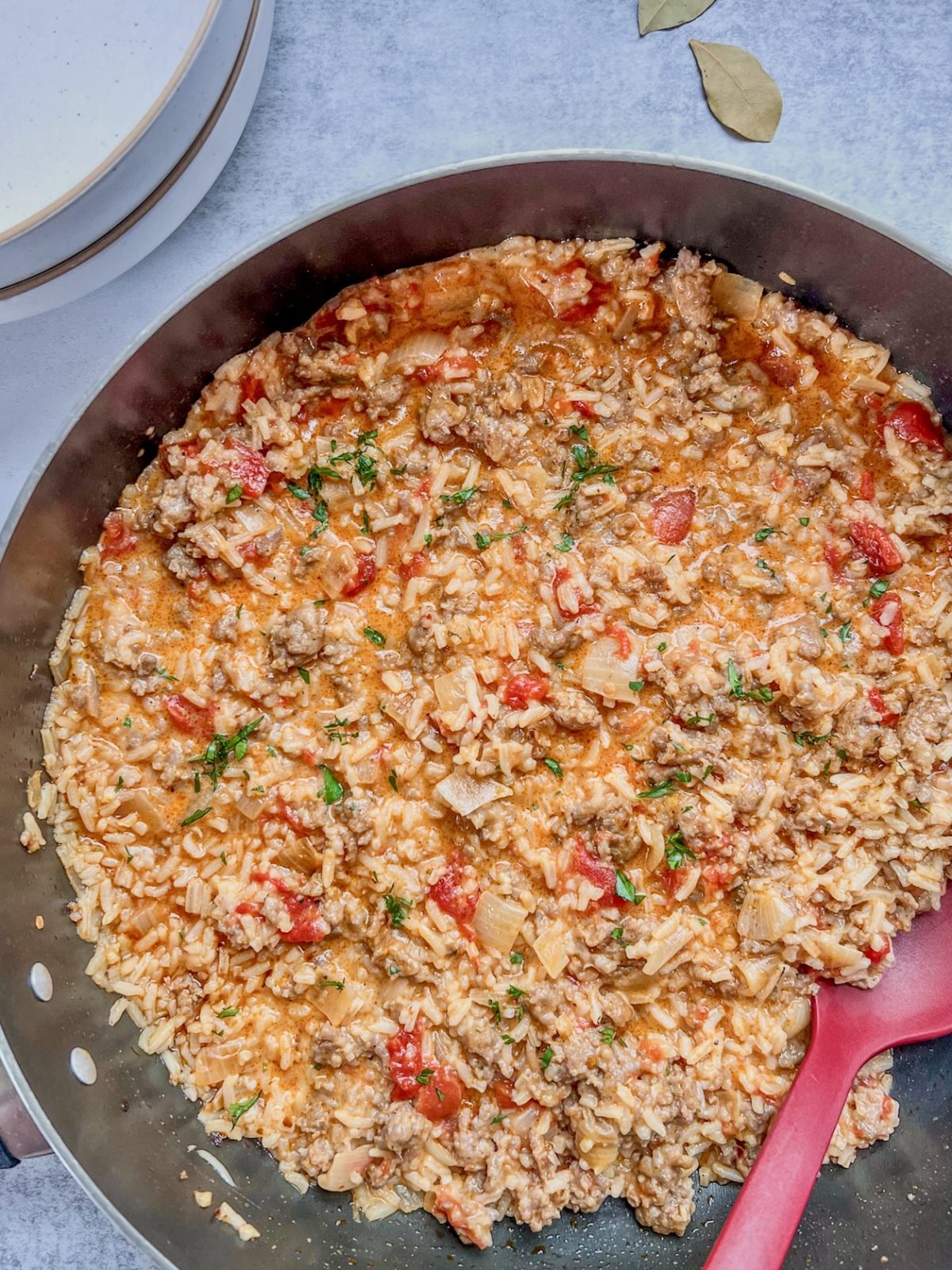 Sausage and tomato rice skillet in a pan with fresh parsley on top and bowls on the side