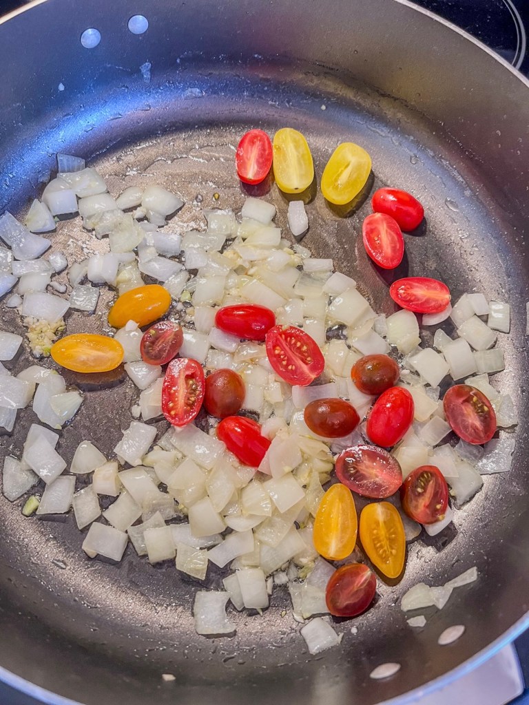 Onion, garlic, and tomatoes cooking in a skillet on the stove